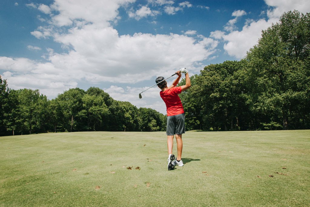 Youth golfer hitting approach shot from tee box