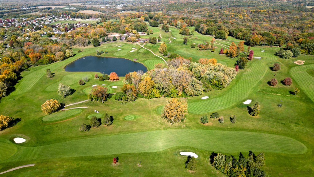 Bird's eye view of golf course with manicured greens trees and pond